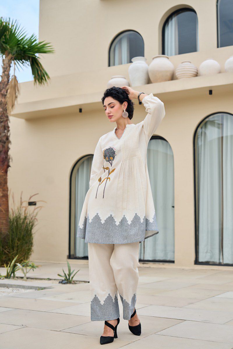 Woman in a stylish outfit standing in front of a modern building with decorative elements.