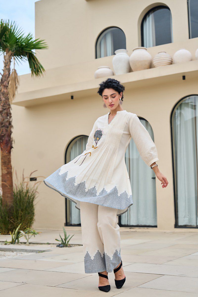 Woman in a cream and gray traditional outfit standing in front of a building with decorative vases.