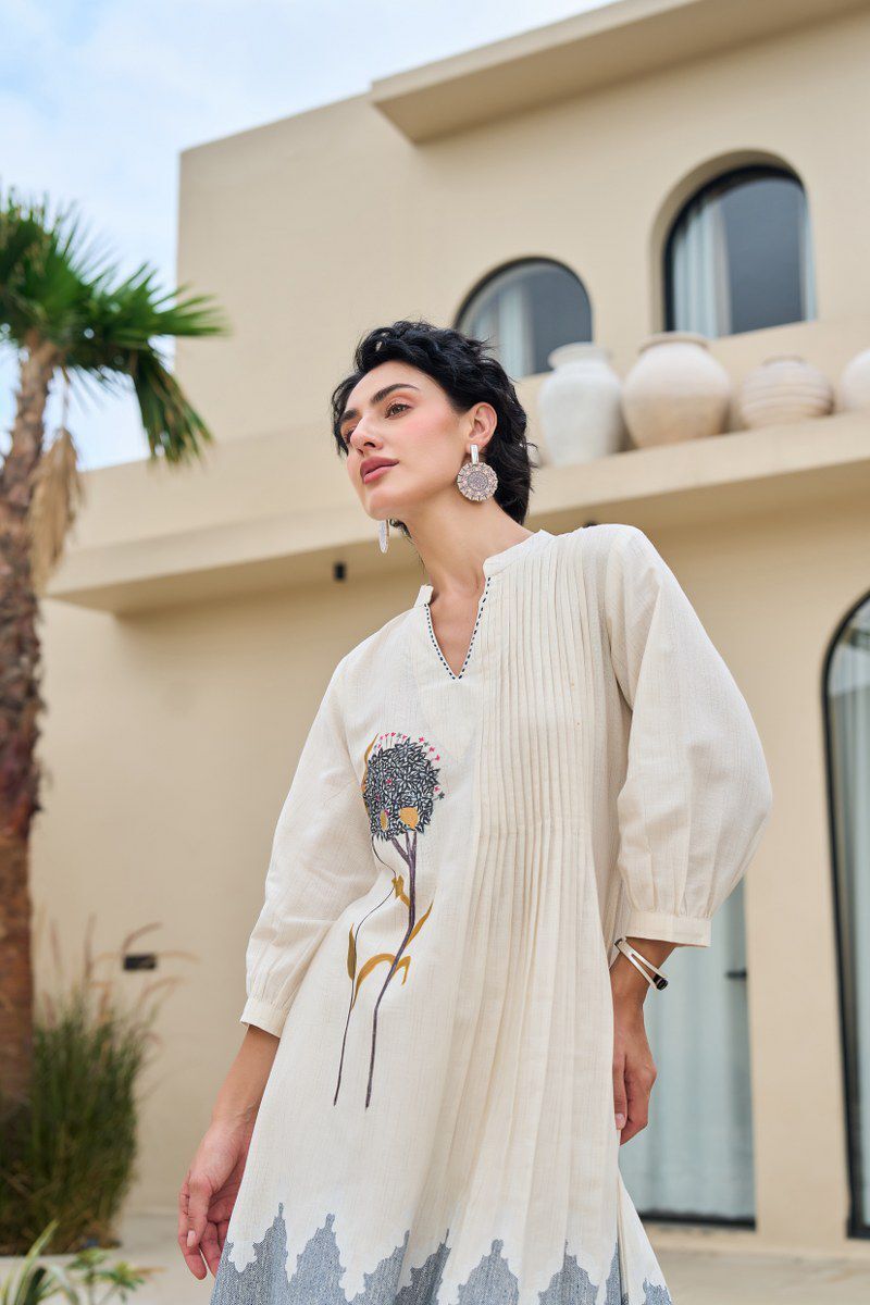Woman wearing a white dress with floral design in front of a building.