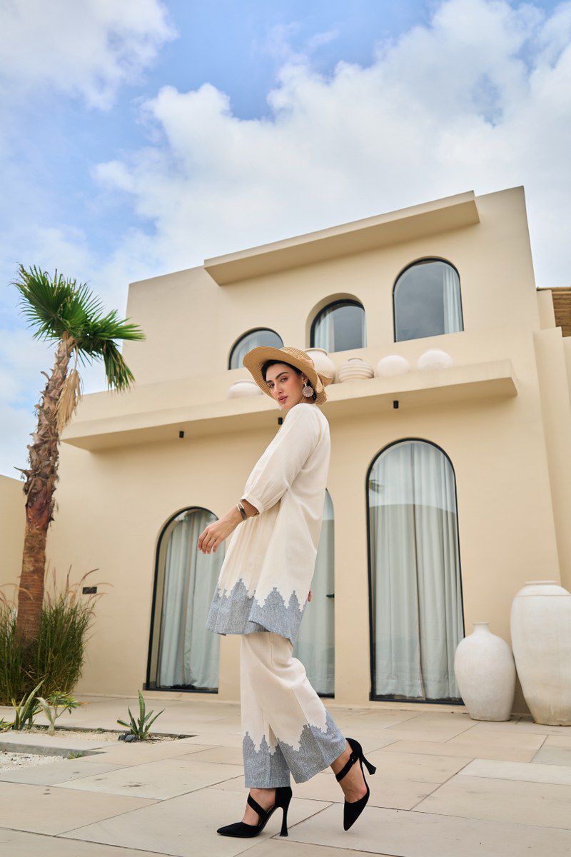 Woman in a stylish outfit standing in front of a modern building with a palm tree.